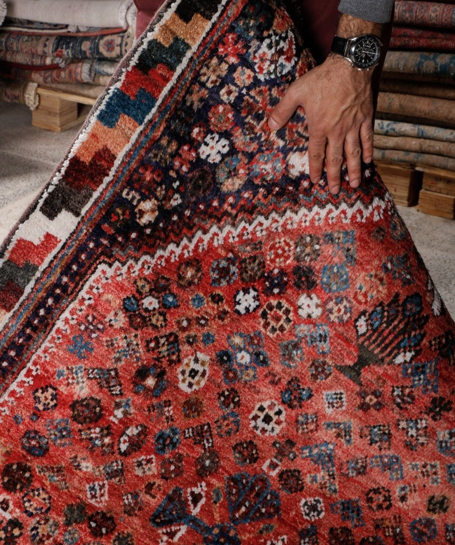 Persian-style rug lifted by hand; red field with blue and white motifs and dark border