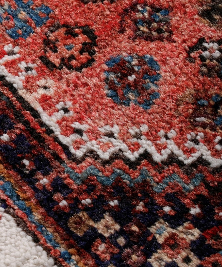 Persian-style rug corner close-up with red, blue, and cream geometric patterns and textured pile