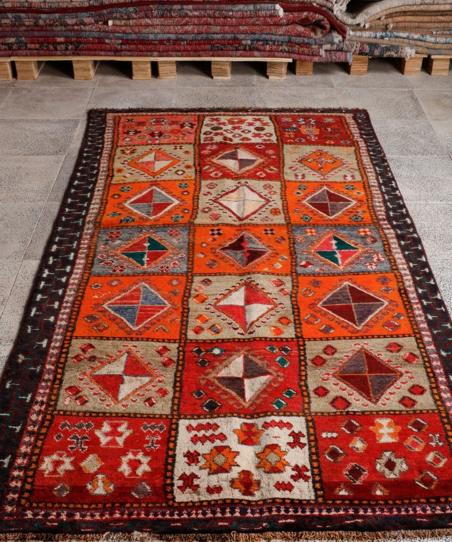 Persian Shiraz rug lying flat, red-orange geometric panels with cream diamonds and dark border.