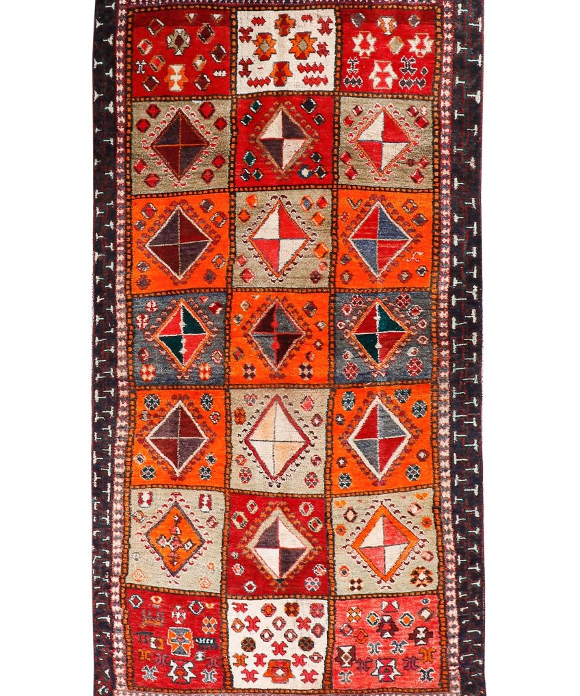 Persian Shiraz rug with red-orange field, cream diamonds, navy border and fringe.