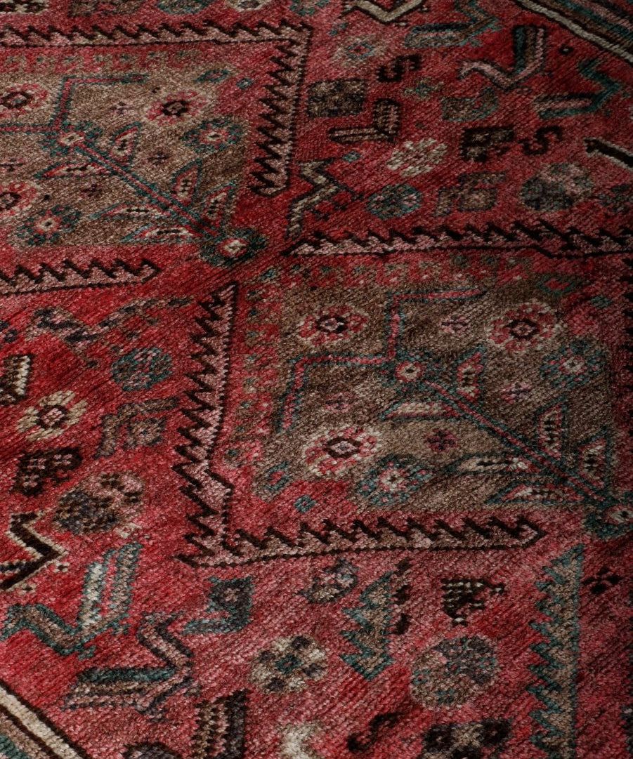 Persian Shiraz rug texture detail, red background with intricate cream and teal motifs.