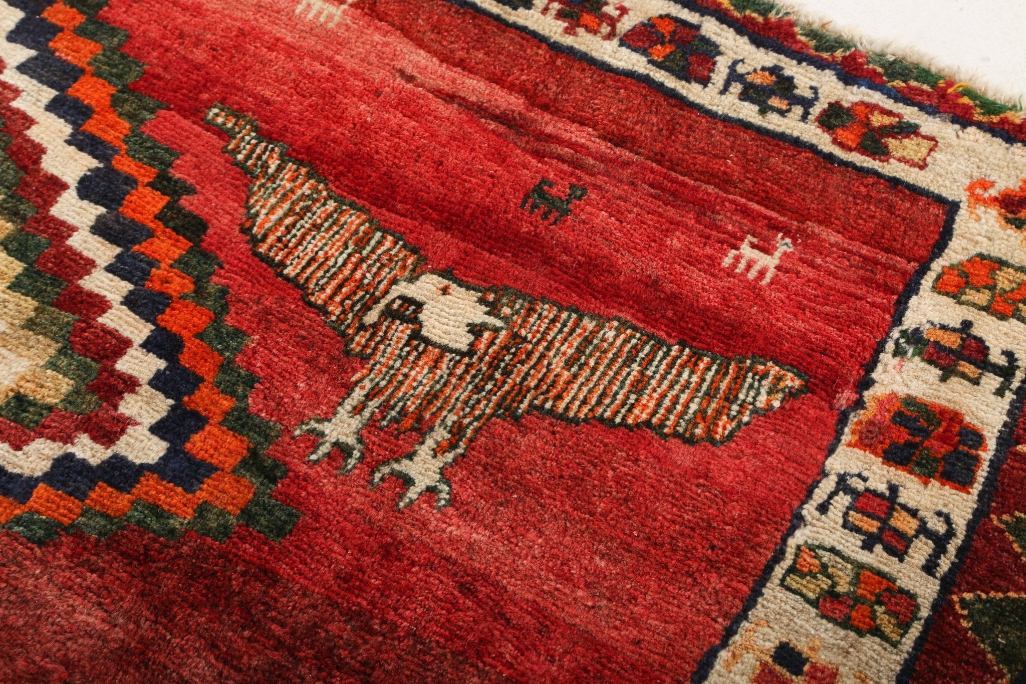 Close-up of red rug with dense geometric motifs and cream multicolor trim border.