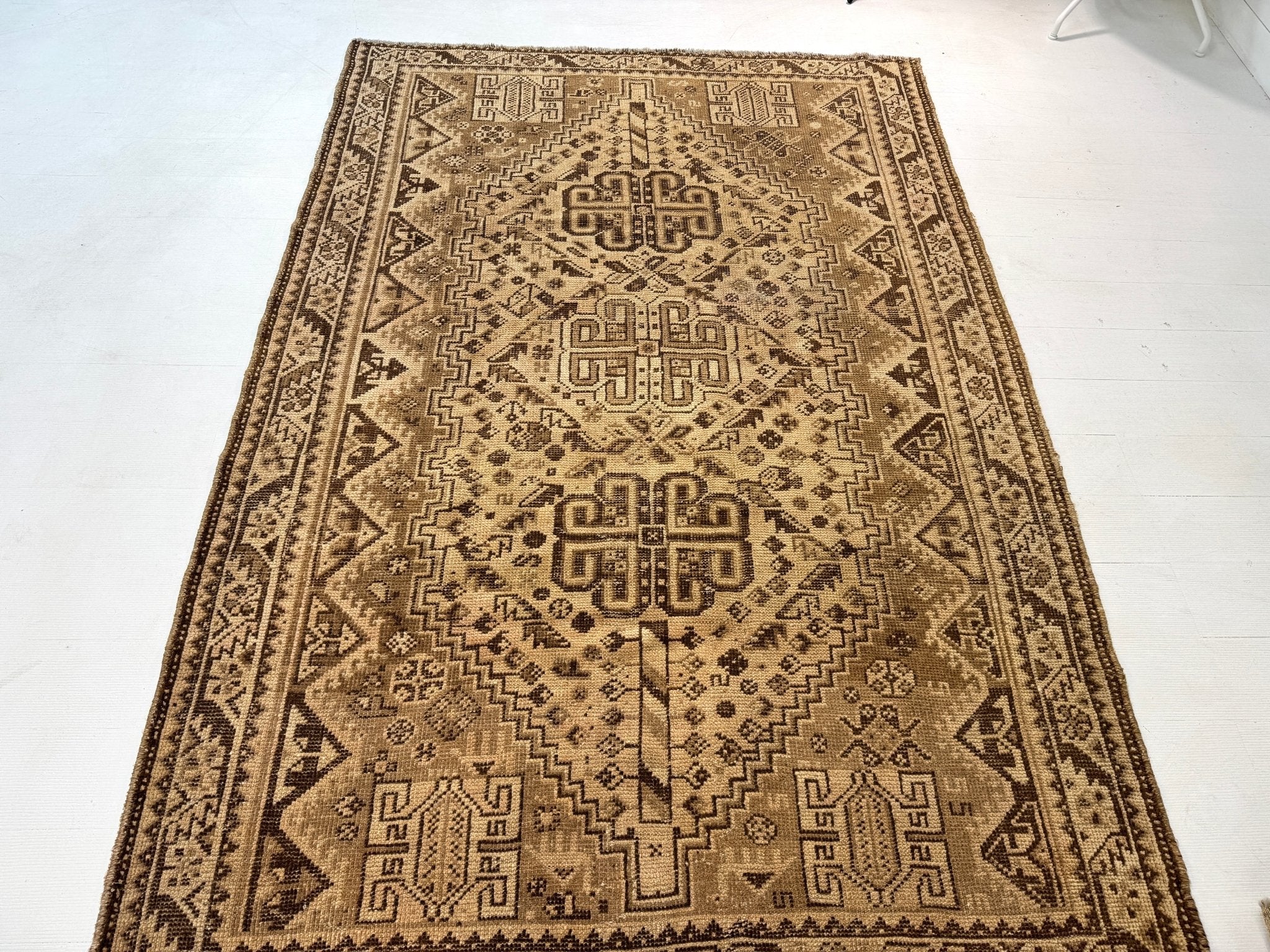 Persian rug in warm tan with dark brown corner details, central medallions, and border trim.