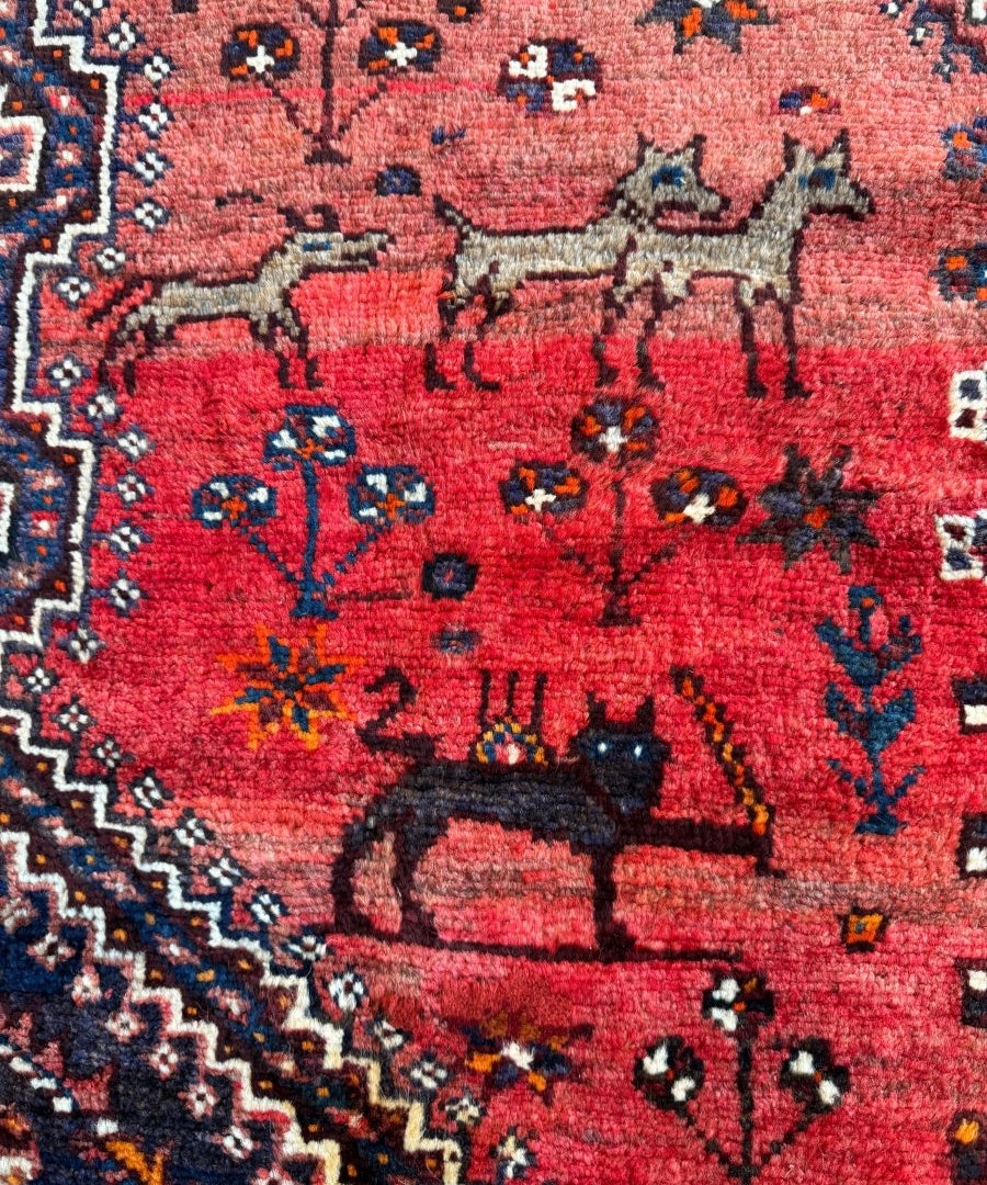 Persian Shiraz rug close-up, red and navy field with animal silhouettes and diamond motifs
