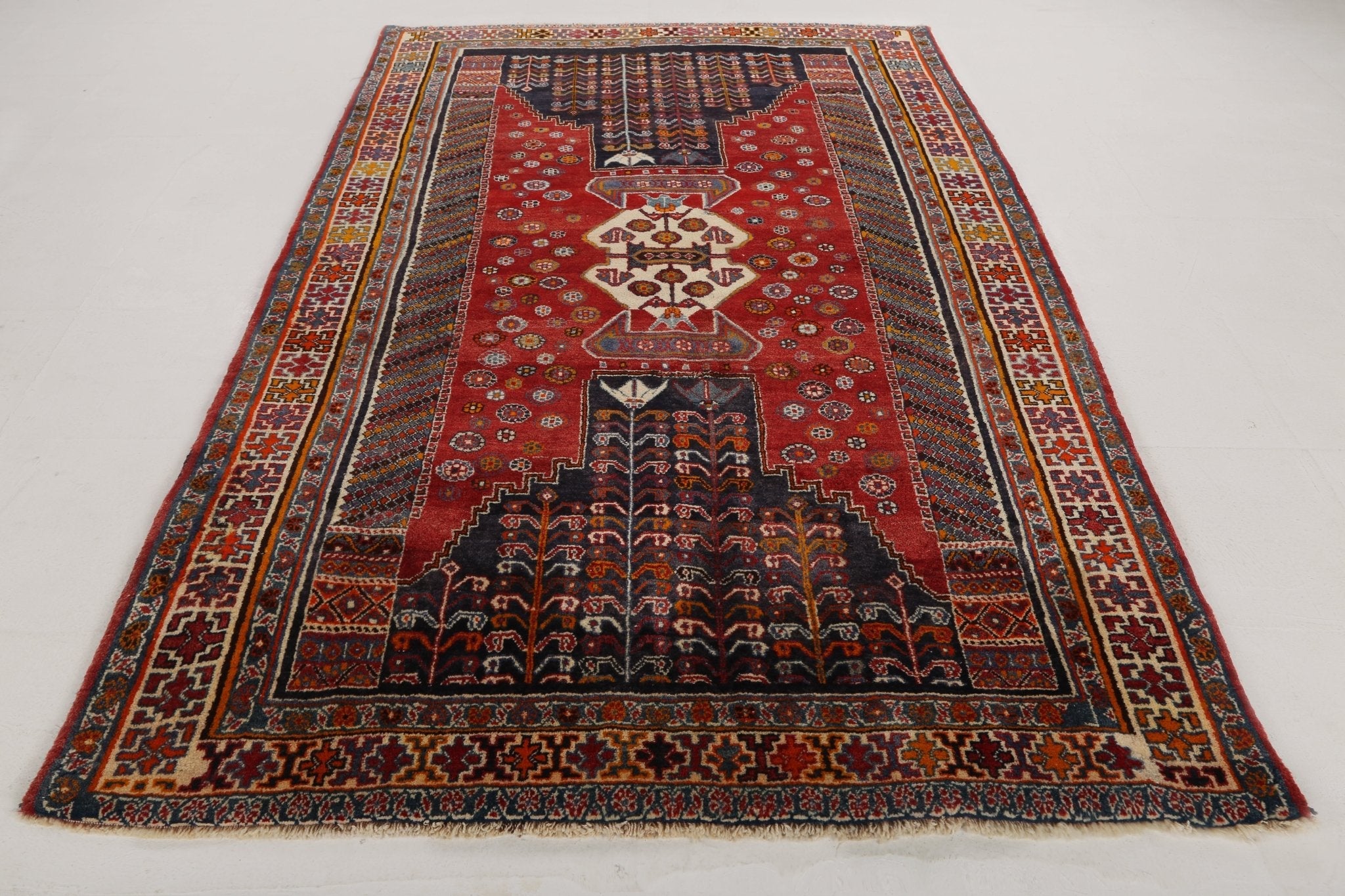 Persian-style rug with red background, central star motif, and dark blue prayer niche design