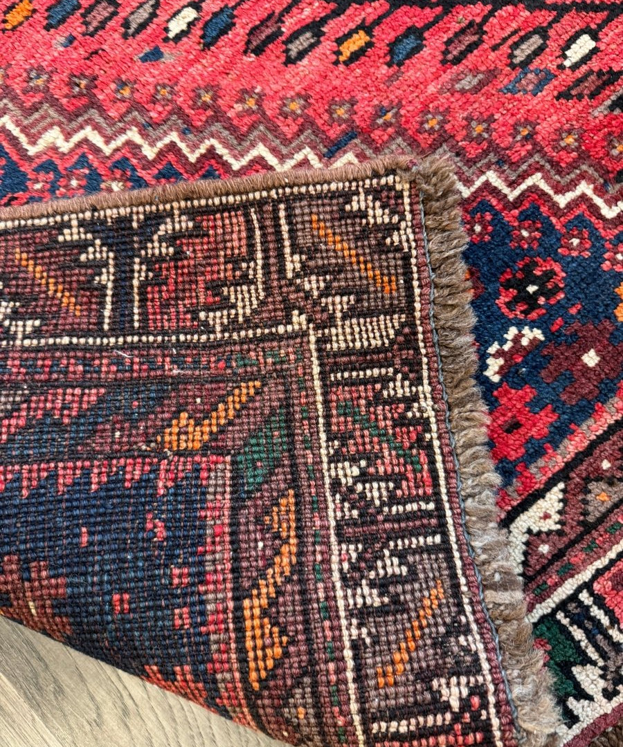 Navy patterned rug section with red accents, cream zigzags and plush fringe trim