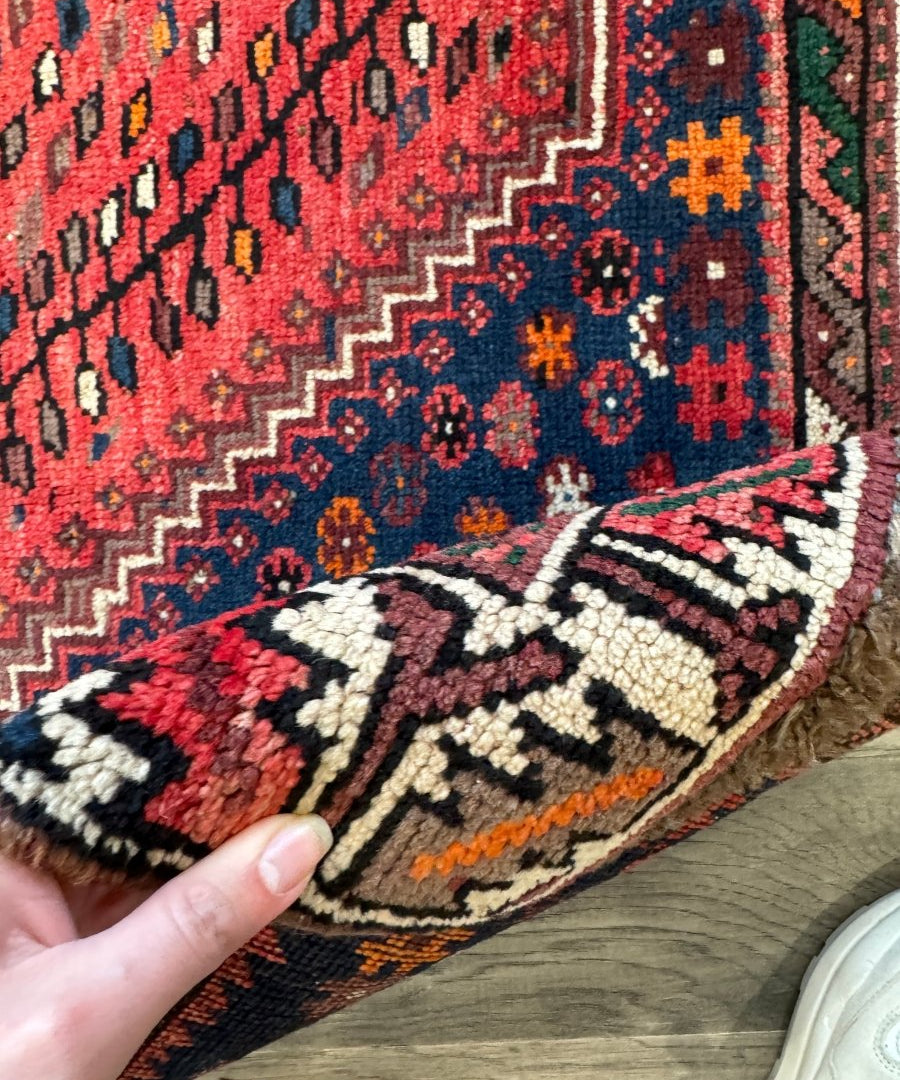 Persian rug corner detail with red and navy motifs, cream outlines and fringe edge