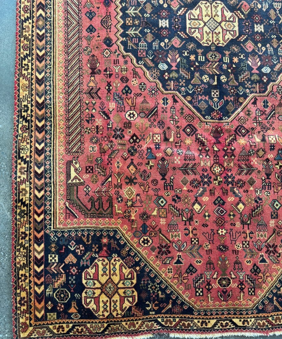 Persian-style rug with red-pink field, navy motifs, and multicolor geometric border