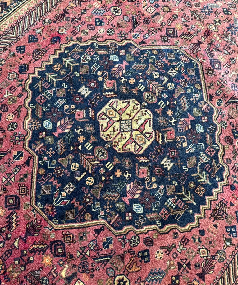 Persian-style rug close-up with red-pink field, navy rosette medallion, cream accents
