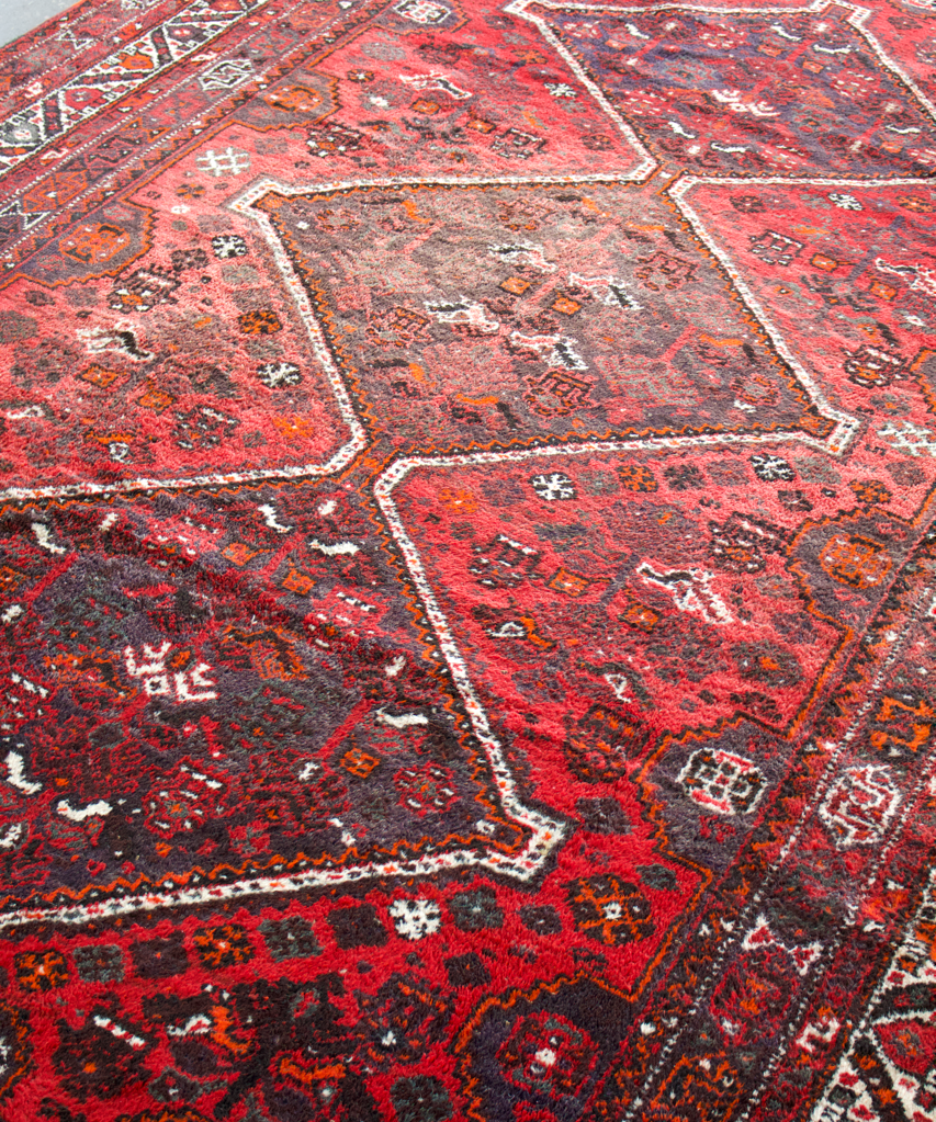 Persian Shiraz rug close-up from above, red medallions with gray detailing and border trim.