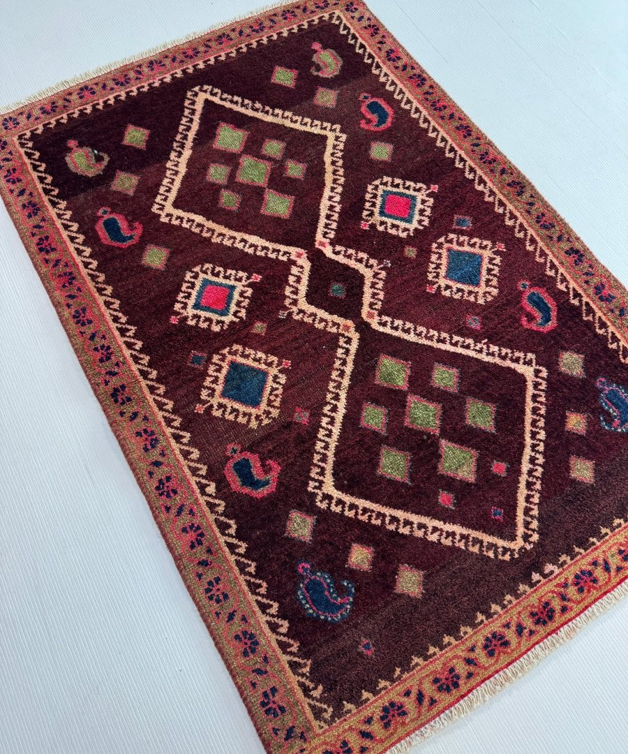Geometric Persian-style rug in dark burgundy with multicolor motifs and patterned border.