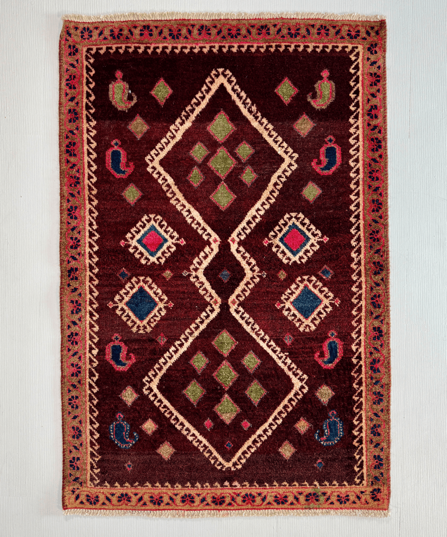 Square rug with dark burgundy background and multicolor geometric diamond pattern.
