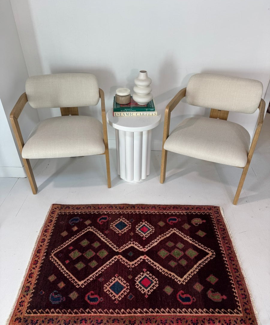 Persian-style area rug with dark burgundy field, geometric diamond medallions, red border.