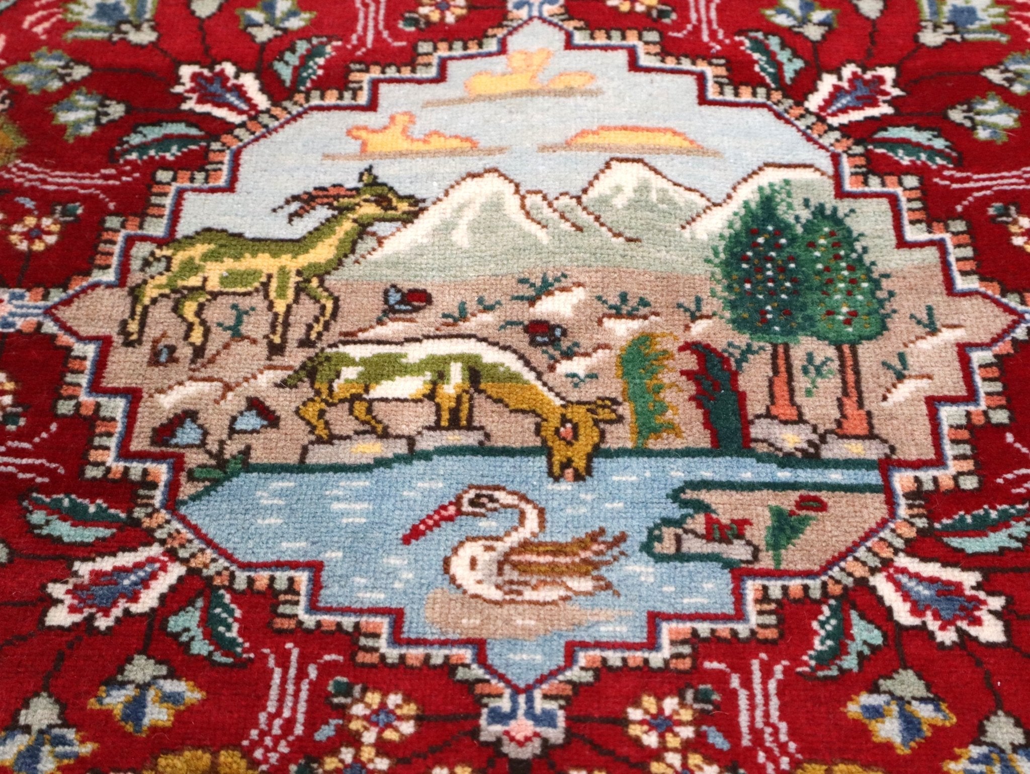 Close-up of Persian Tabriz rug landscape medallion, red field with multicolor details.