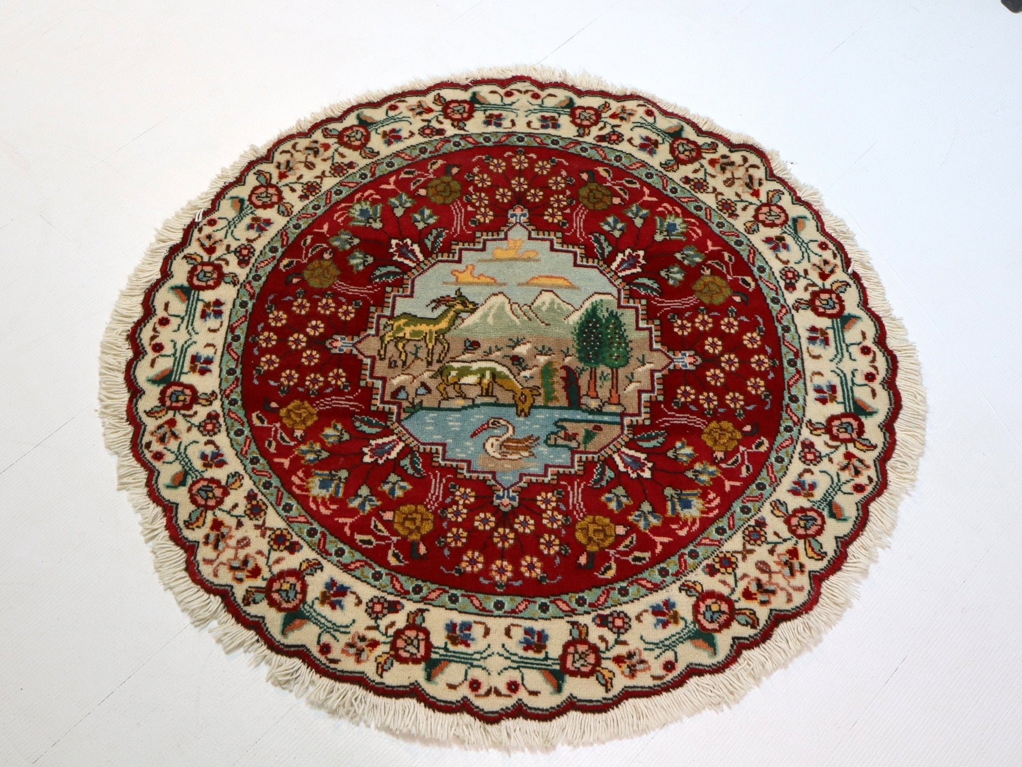 Round Persian Tabriz rug with red medallion, animal scene, cream ornamental border, fringe.
