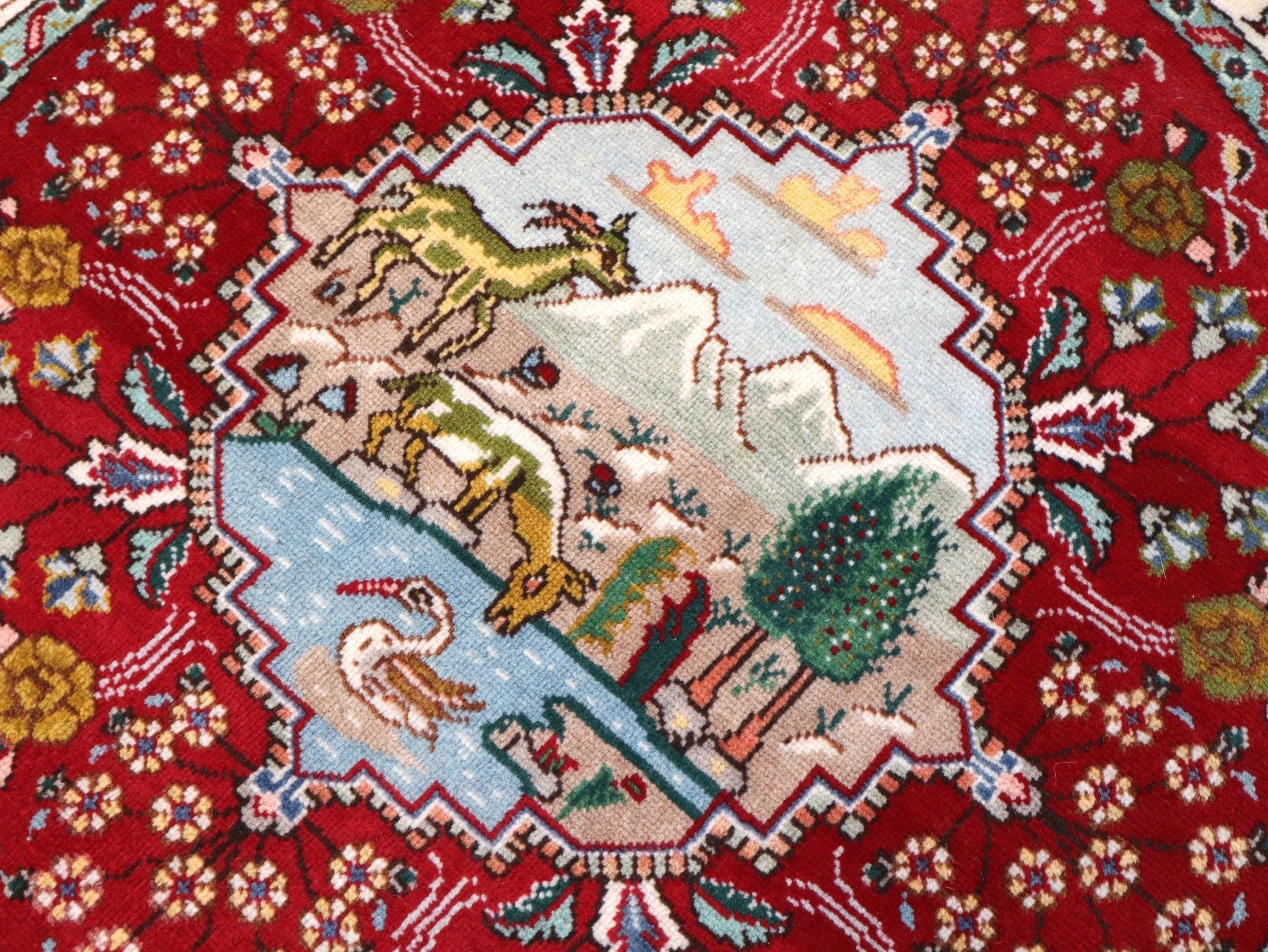 Close-up of Persian Tabriz rug with village landscape, red background, intricate border.
