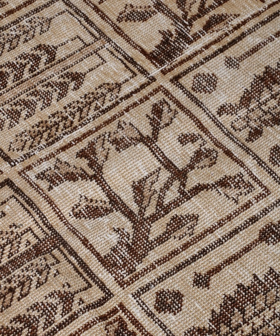 Close-up of beige rug with dark brown cross-banded pattern and small decorative motifs.