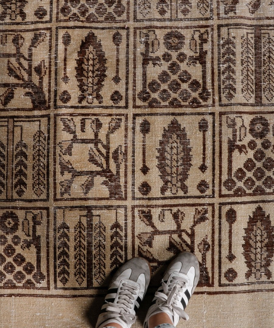 Beige Persian-style rug corner with dark brown geometric medallions; textured woven pile.