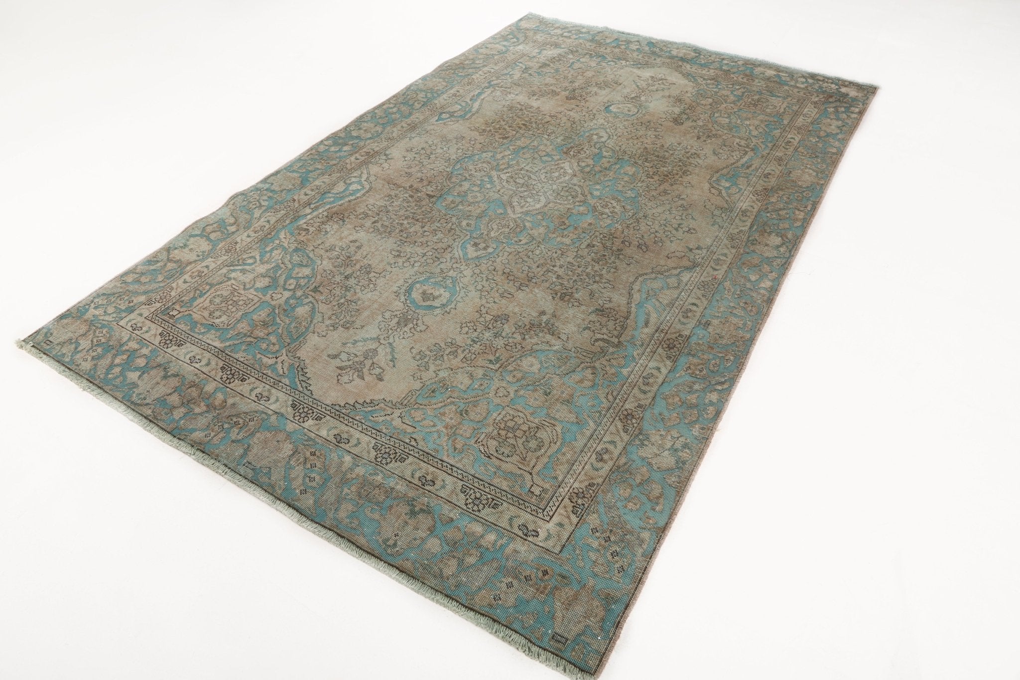 Persian Tabriz rug laid flat, beige field with teal ornamental border and motifs