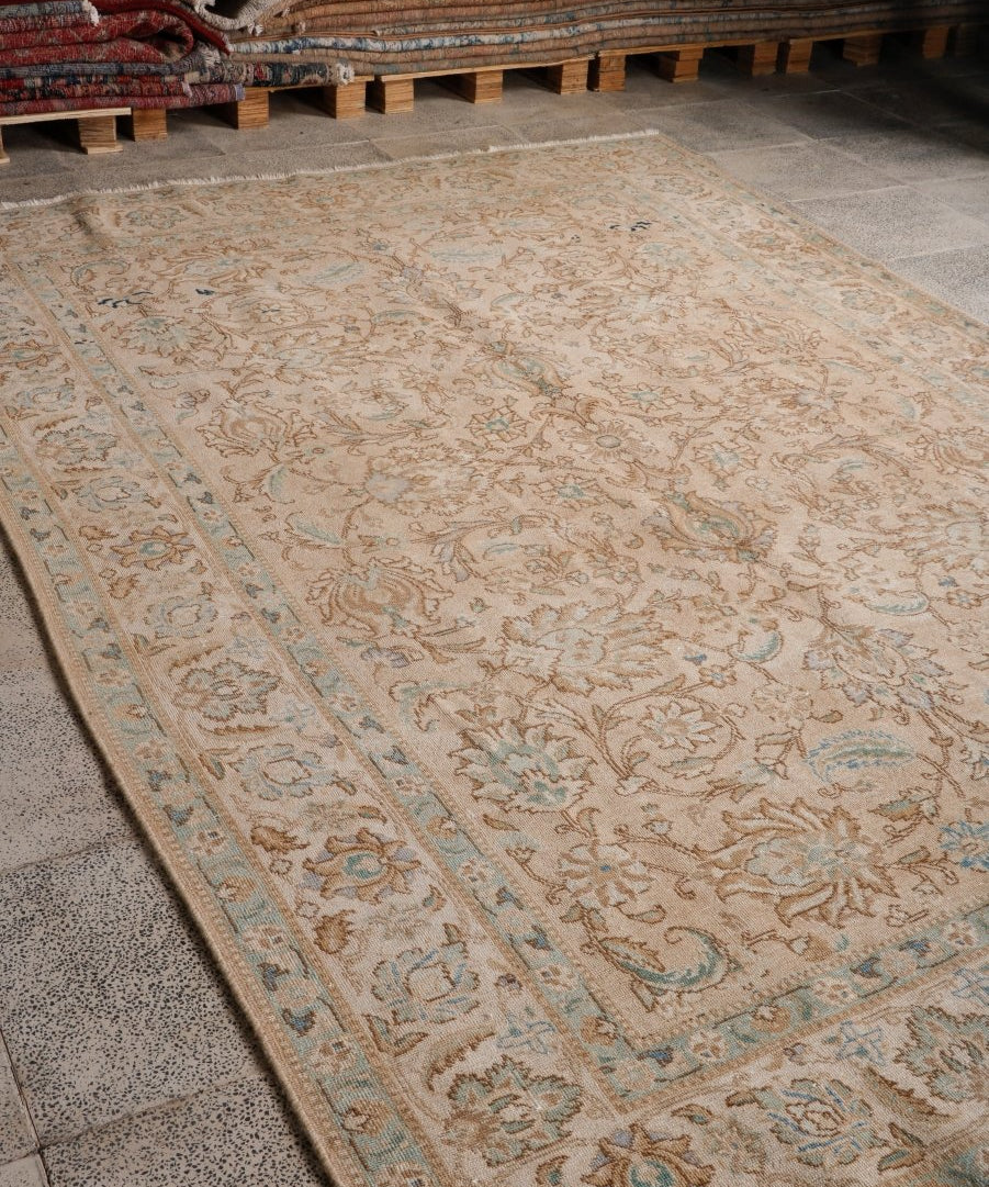 Tabriz-style rug laid flat; beige field with teal floral border and intricate medallion motifs.