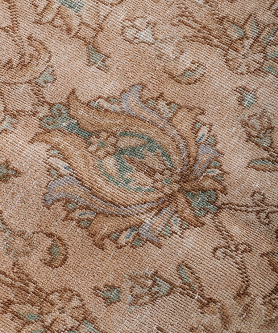 Close-up of beige rug weave with teal floral accents and fine ornamental pattern lines.