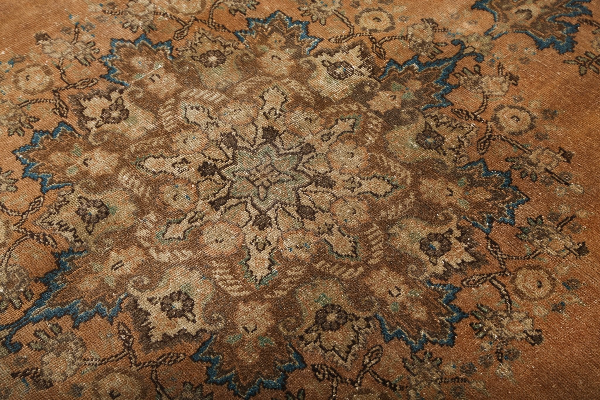 Close-up Persian rug with rust ground and dense beige, teal, and dark patternwork
