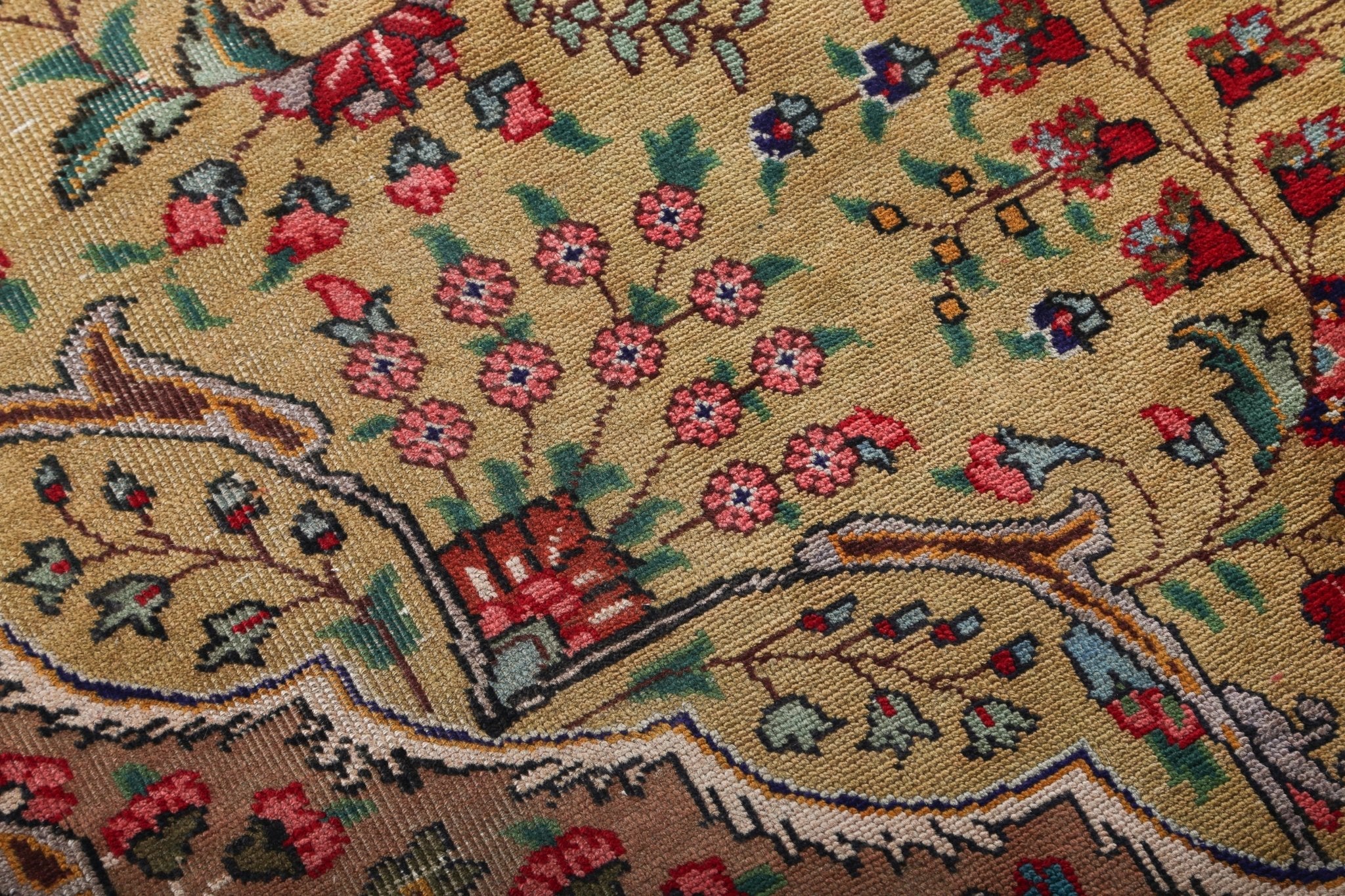Persian Tabriz rug close-up with flower and leaf motifs in red, blue, and green on beige