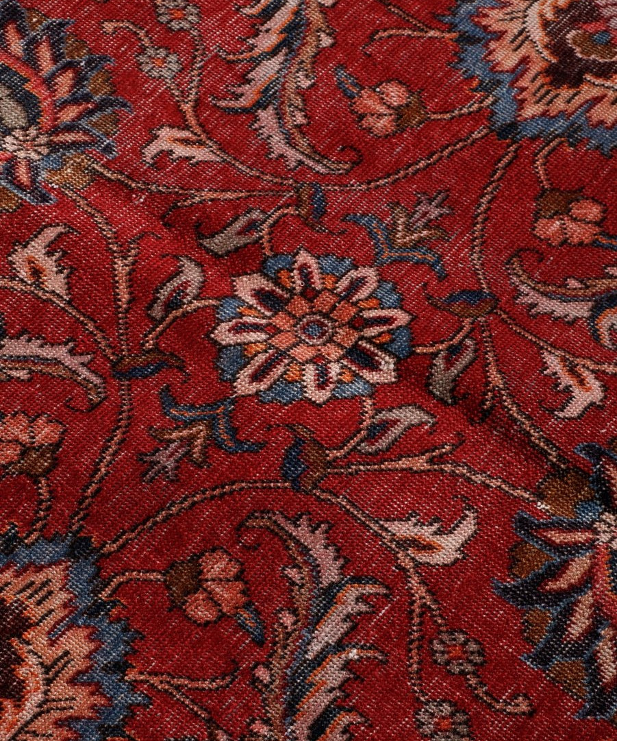 Red rug surface detail with scrolling vines, floral rosettes, and geometric accents.