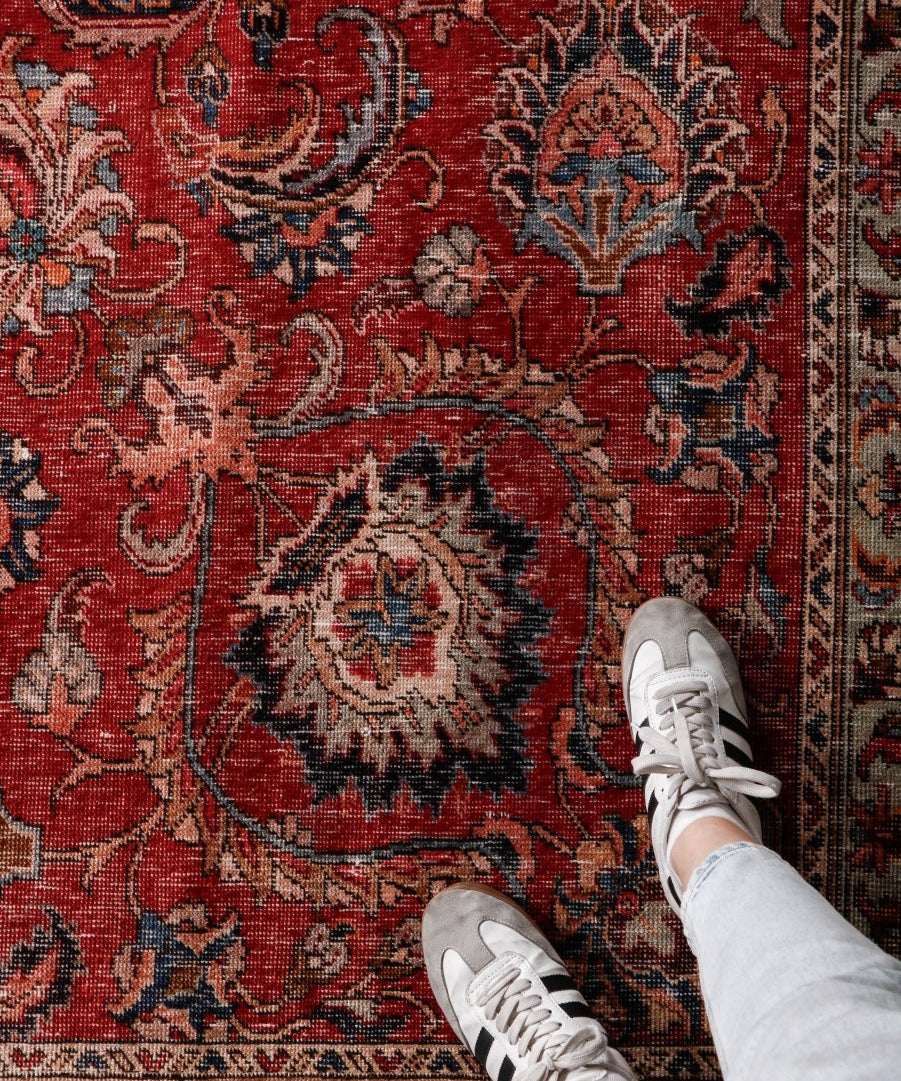 Red rug close-up with detailed floral motifs, central medallion, and decorative border.