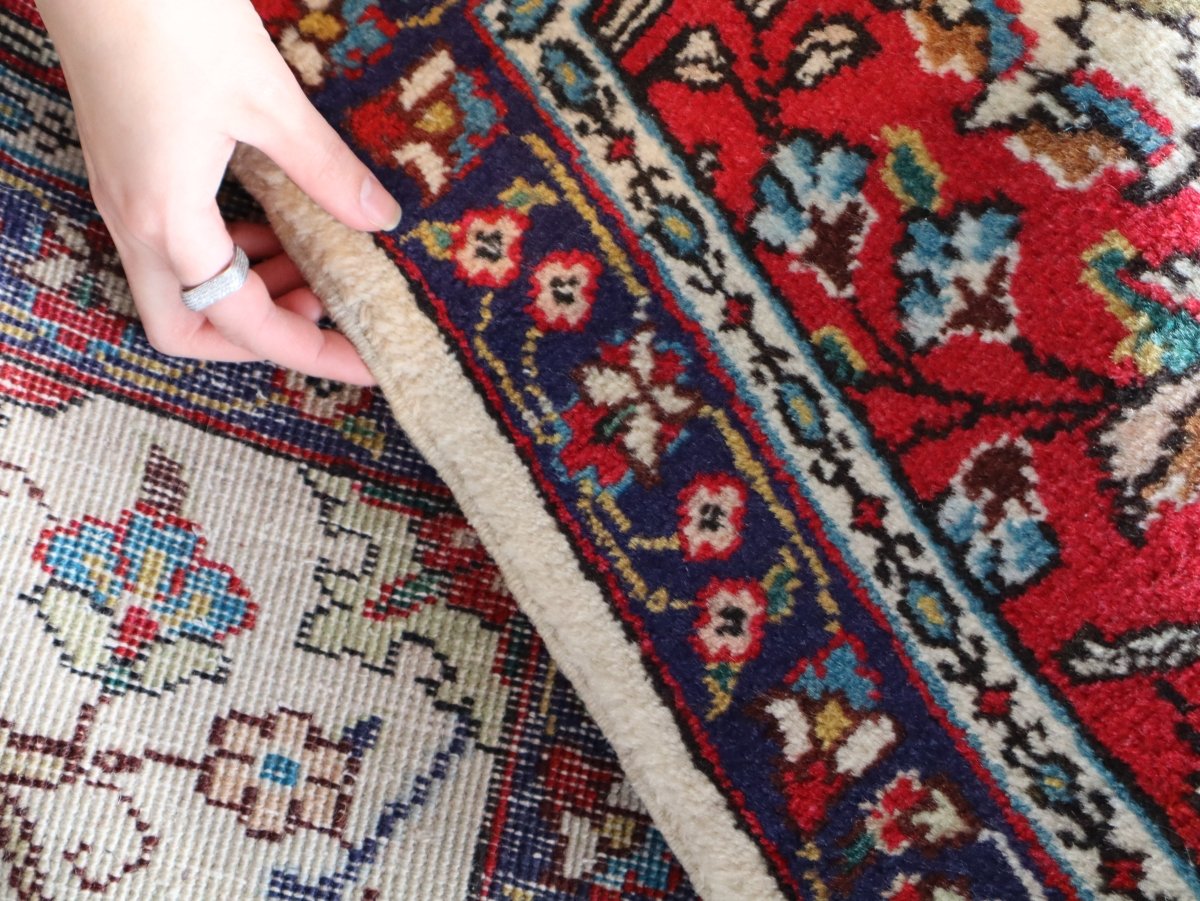 Close-up of patterned rug edge with red and blue motifs and cream fringe detail.