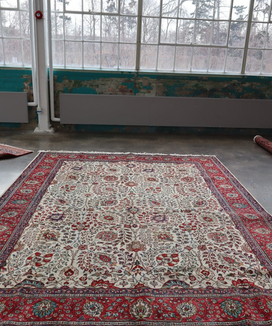 Large area rug featuring cream field with red medallions and navy floral border, fringed.