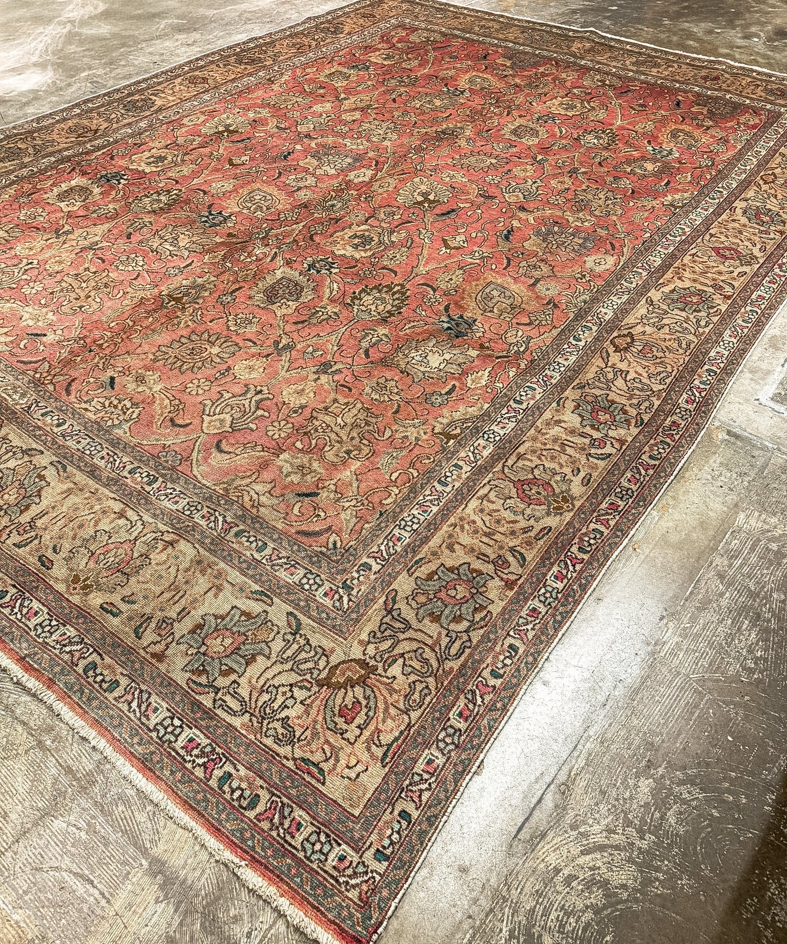 Angled rectangular rug with coral red center, beige-gray border, and intricate floral designs