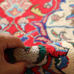 Persian Tabriz rug texture detail; hand shows woven pile on red and blue patterned area