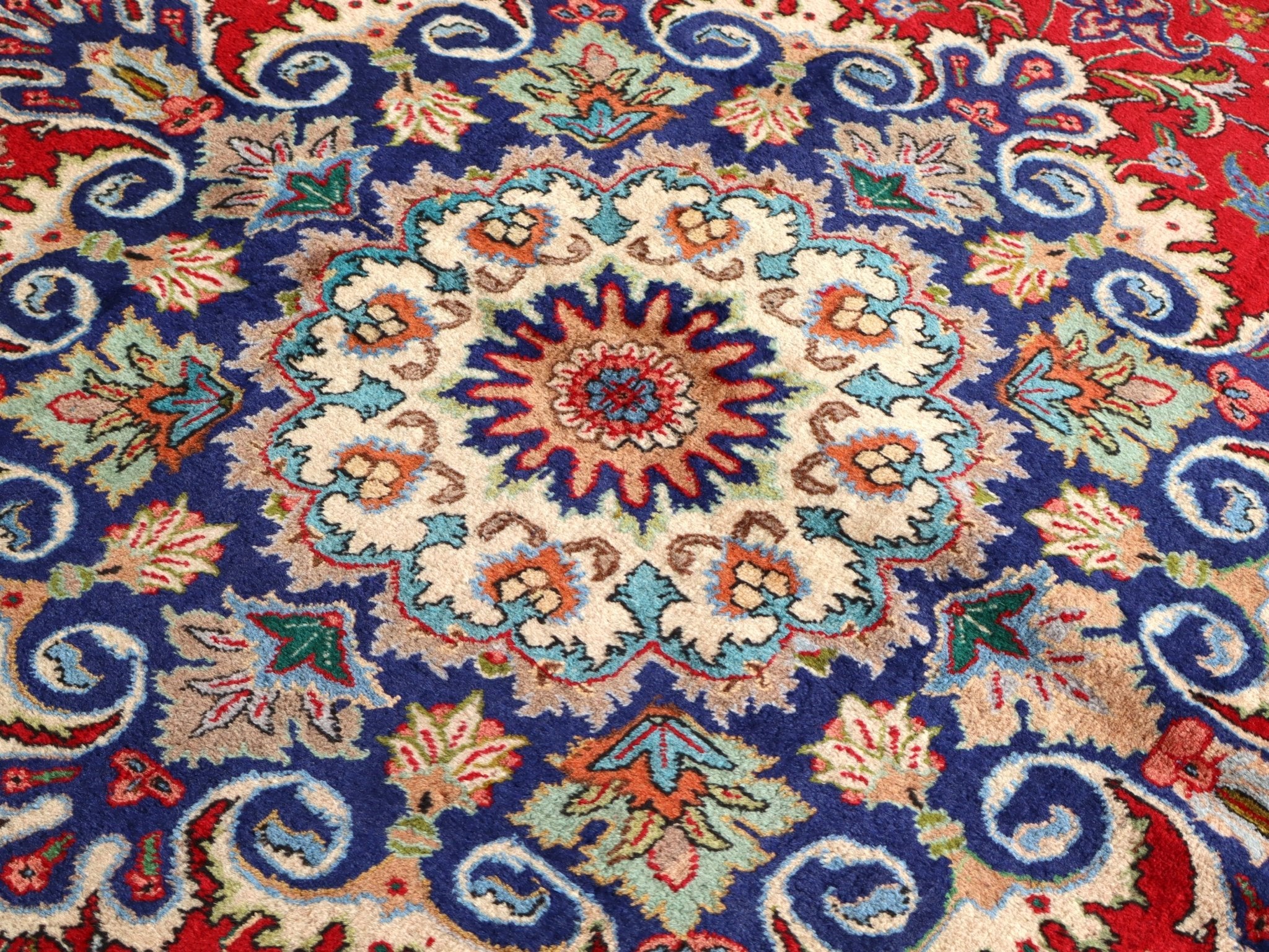 Persian Tabriz rug with navy medallion design on red-blue ground and floral accents