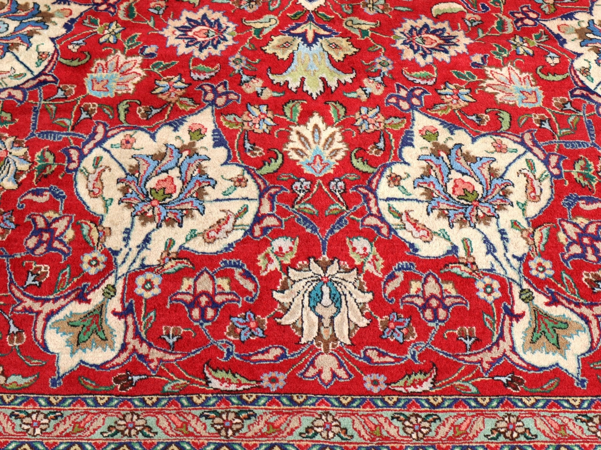 Persian Tabriz rug close-up of red field, blue motifs, and cream scrollwork border