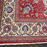 Persian Tabriz rug corner close-up with fringed edge, red border, and cream floral panels