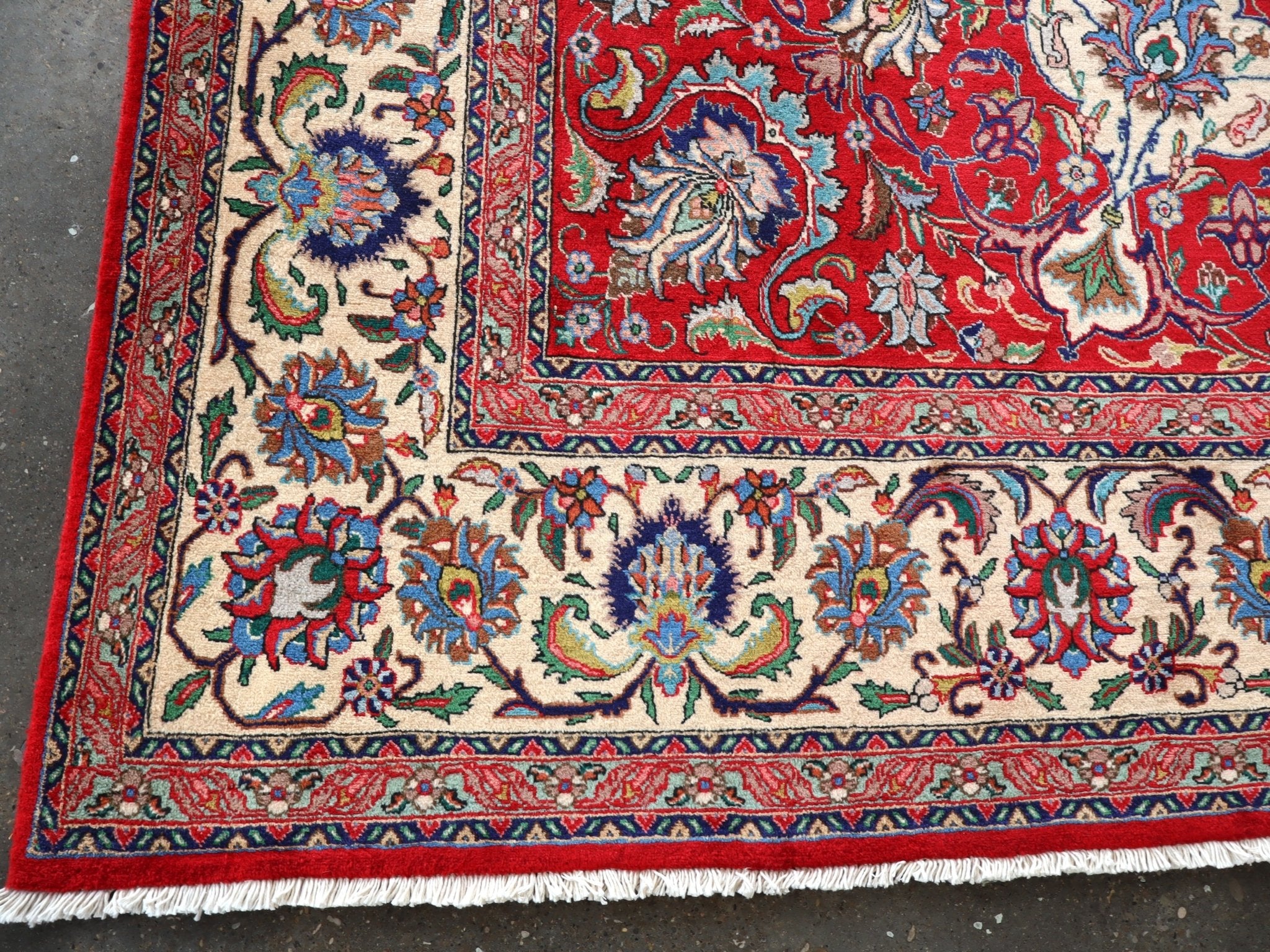 Persian Tabriz rug corner close-up with fringed edge, red border, and cream floral panels