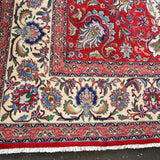 Persian Tabriz rug corner close-up with fringed edge, red border, and cream floral panels