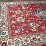 Persian Tabriz rug corner view, red field with cream border and blue floral details