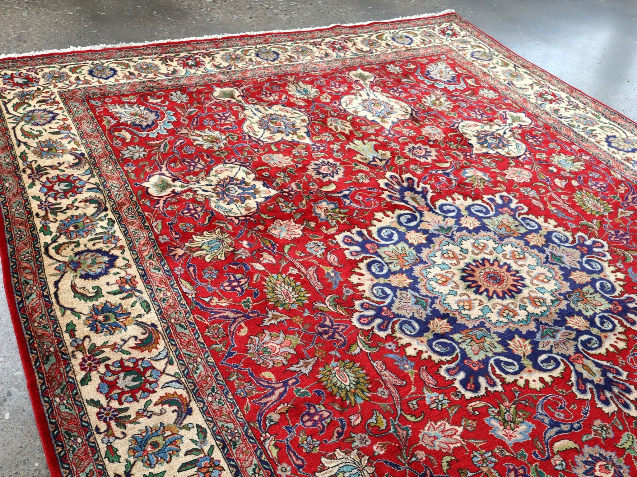 Persian Tabriz rug angled view with red field, cream-blue medallion, and patterned border