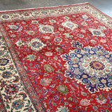 Persian Tabriz rug angled view with red field, cream-blue medallion, and patterned border