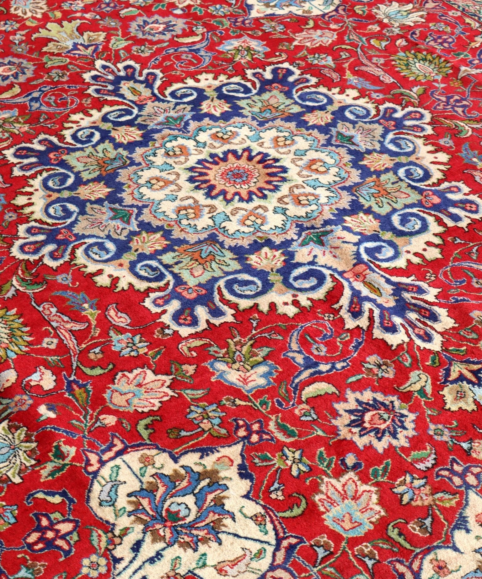Persian Tabriz rug with red field, blue floral medallion, and detailed curving motifs