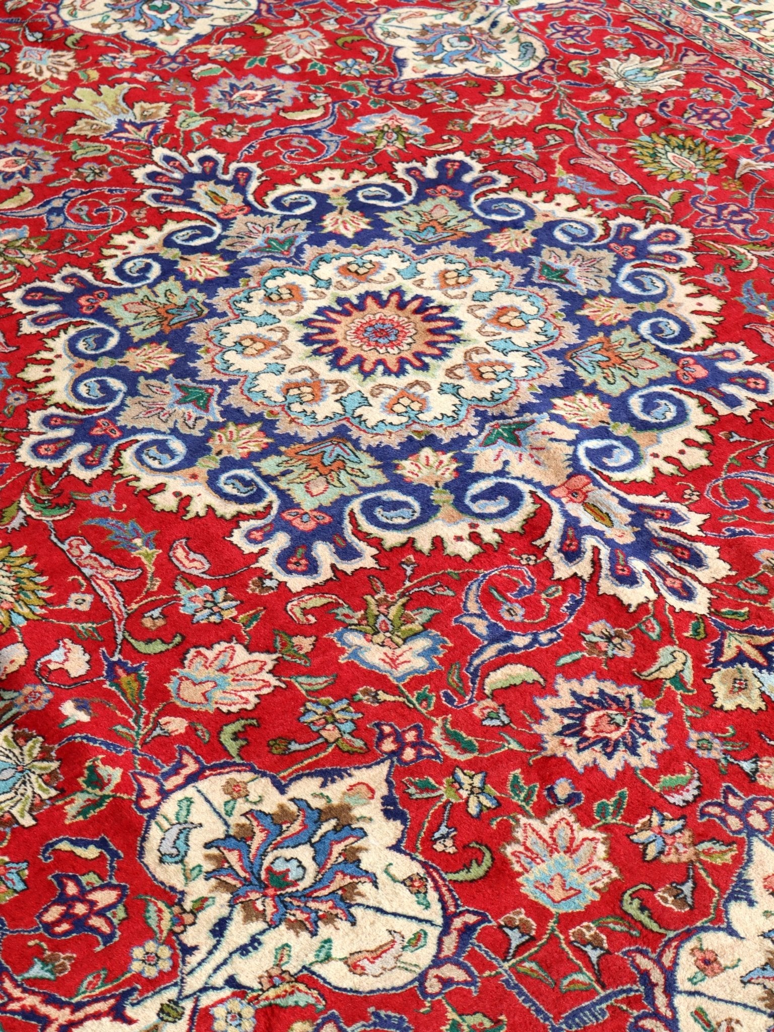 Persian Tabriz rug with red field, blue floral medallion, and detailed curving motifs