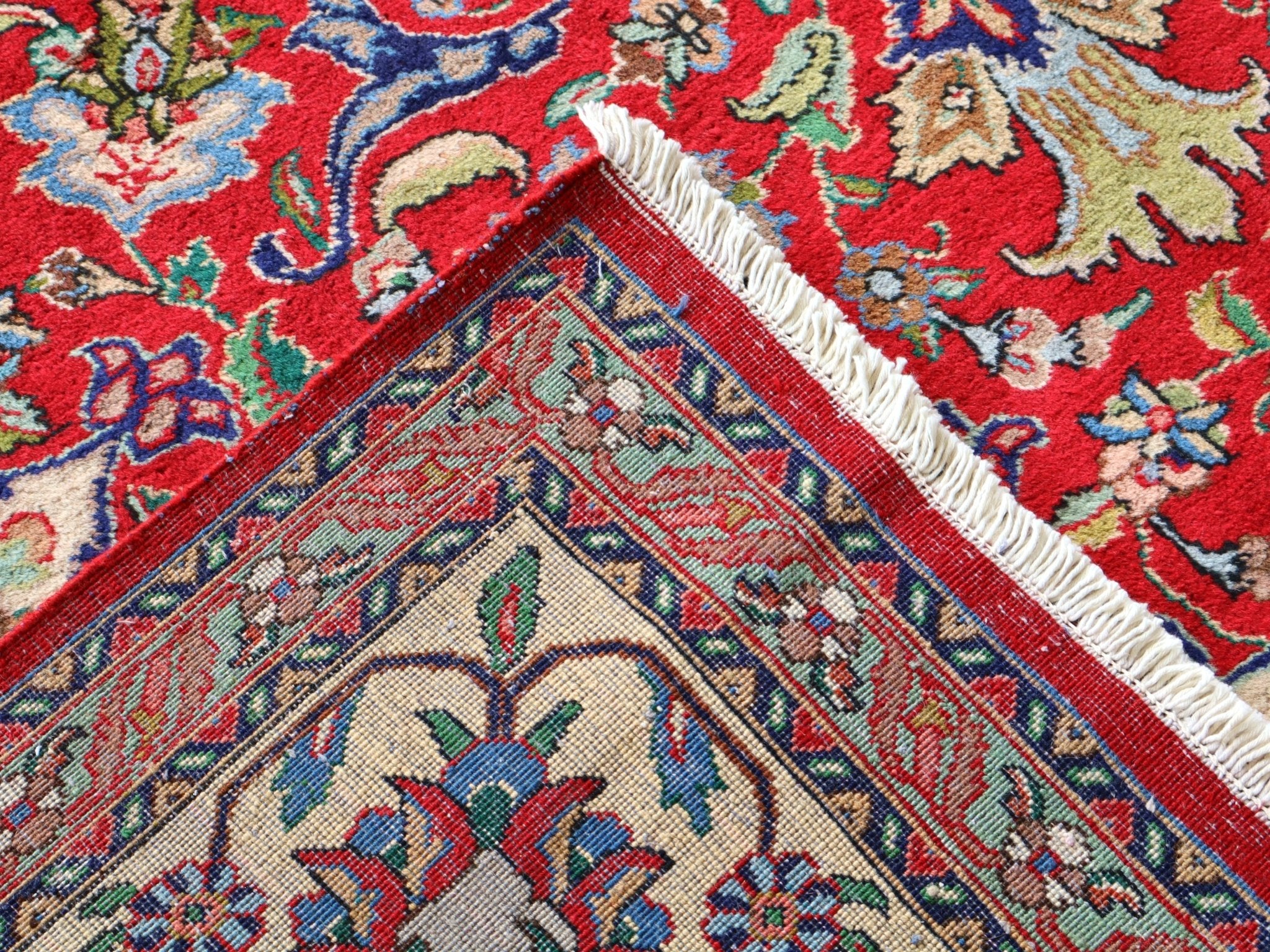 Persian Tabriz rug corner view with fringed cream edge and red-blue geometric border