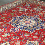 Persian Tabriz rug with red base and large central blue medallion surrounded by florals