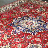 Persian Tabriz rug with red base and large central blue medallion surrounded by florals