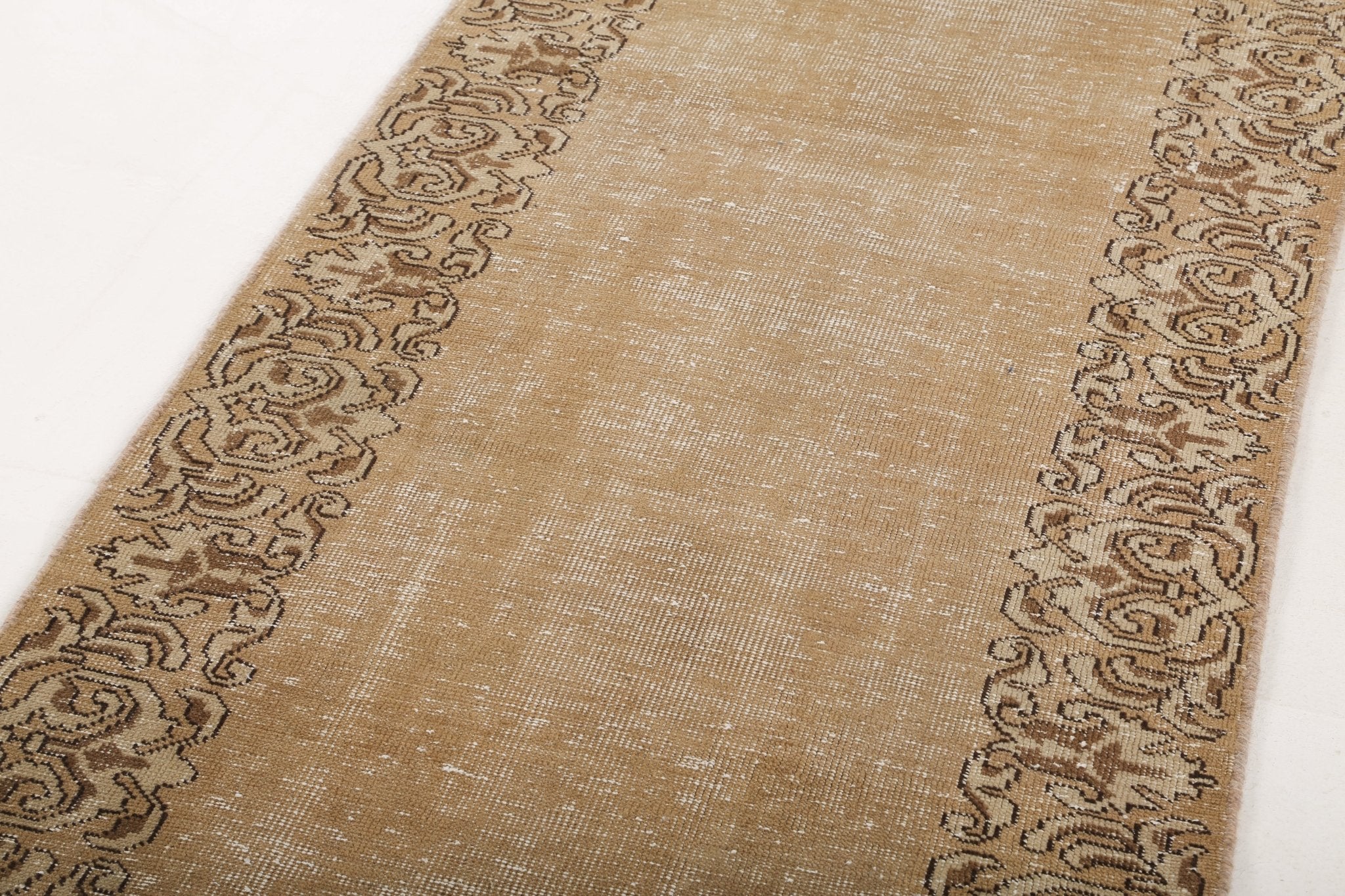 Tan runner rug with dark ornamental border and subtle center field pattern