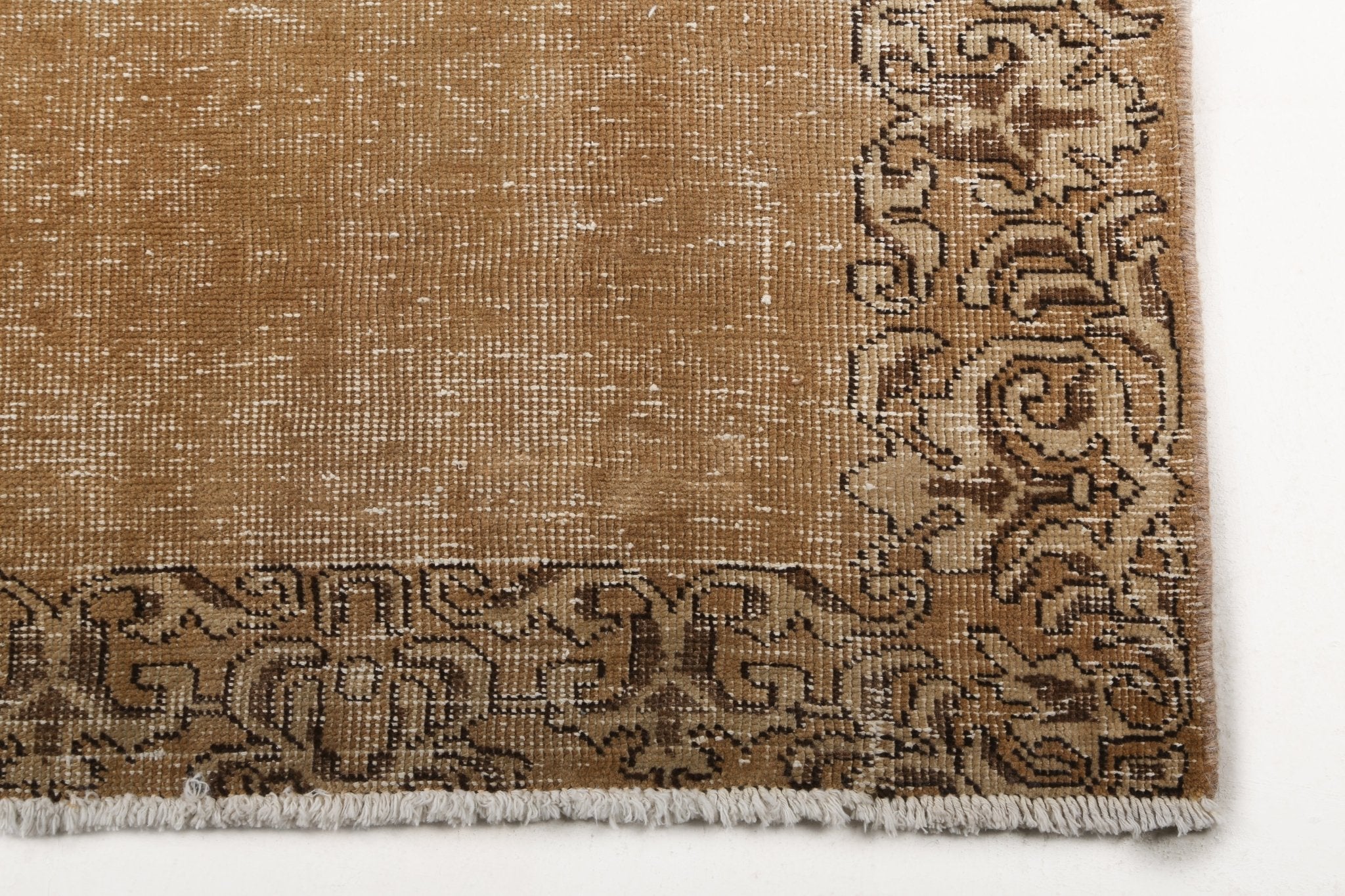 Corner of tan runner rug with dark scrolling border and short fringe edge