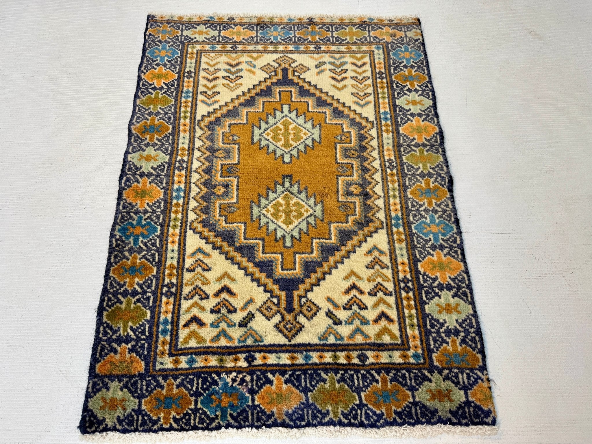 Turkmen rug with cream background, navy border, and tan-and-blue diamond centerpiece