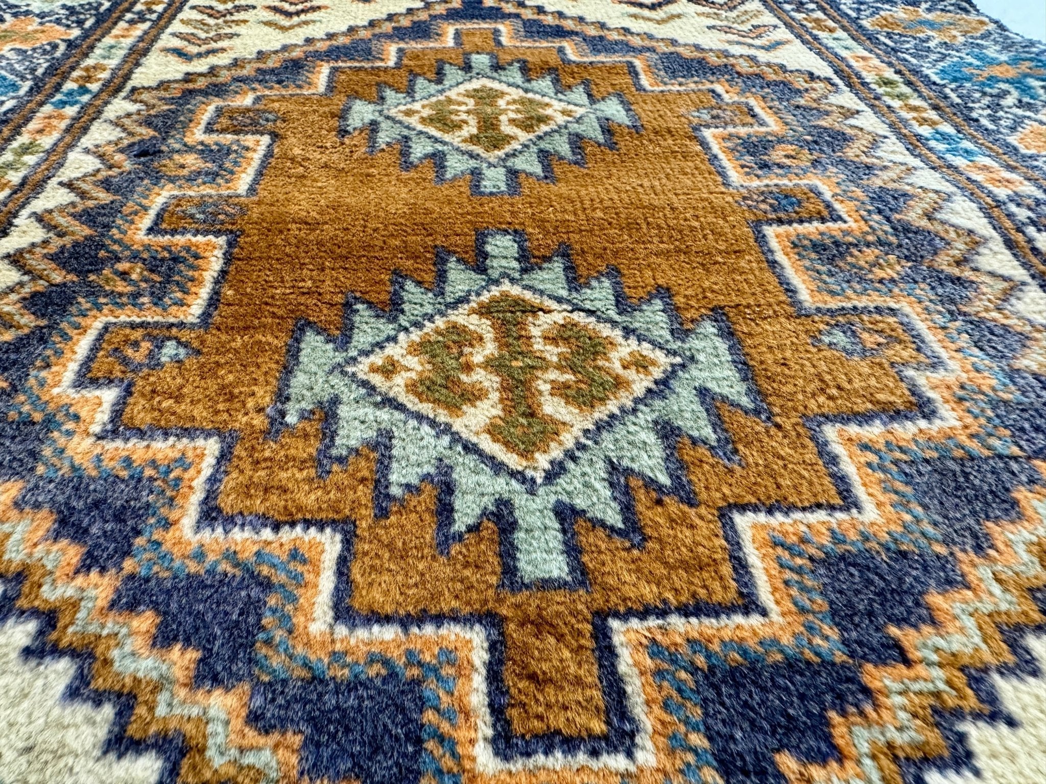 Persian Turkmen rug with warm tan center medallions and blue geometric border